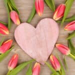 Rosa Herz aus Holz umringt von pinkfarbenen Tulpen